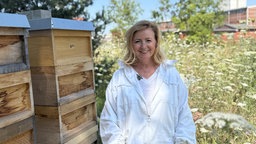 Jutta Lichter im Vordergrund. Im Hintergrund Pflanzen, rechts von Ihr die Bienenstöcke.