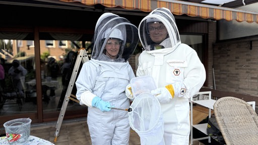 Zwei Personen in Schutzanzügen. Zum Schutz gegen Bienenstiche.