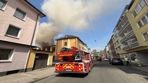 Ein Feuerwehrfahrzeug steht vor einem rauchenden Haus.