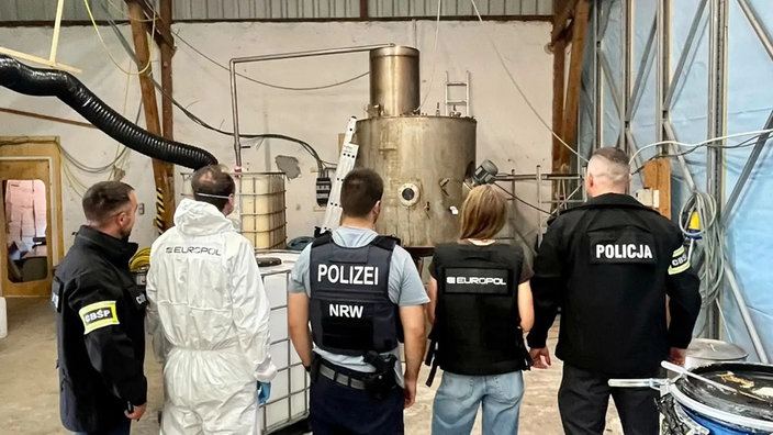 Mehrere Polizeibeamte aus verschiedenen Ländern stehen vor einem Kessel in einer der durchsuchten Lagerhallen.