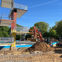 Zwei Bagger und eine Menge an Erdehaufen stehen und den 10 Meter Turm, der sich in Richtung des neuen Beckens richtet. 