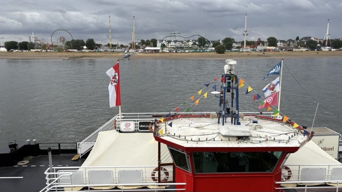 Ansicht auf die Rheinfähre auf dem Rhein. Im Hintergrund die Rheinkirmes.
