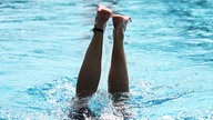 Aus einem Schwimmbecken ragen zwei Beine in die Höhe nach einem Kopfsprung ins Wasser