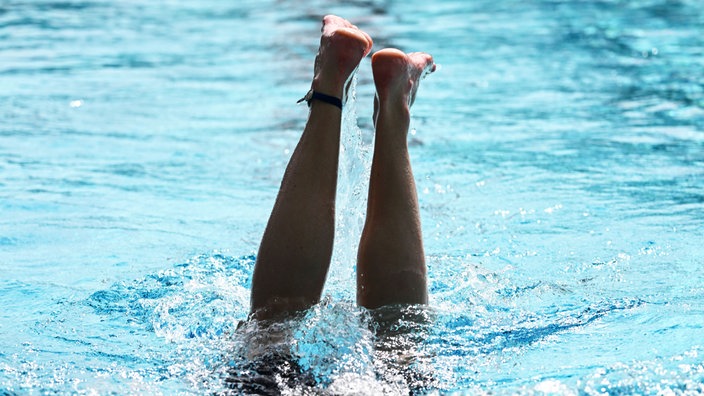 Aus einem Schwimmbecken ragen zwei Beine in die Höhe nach einem Kopfsprung ins Wasser