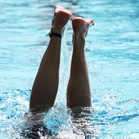 Aus einem Schwimmbecken ragen zwei Beine in die Höhe nach einem Kopfsprung ins Wasser