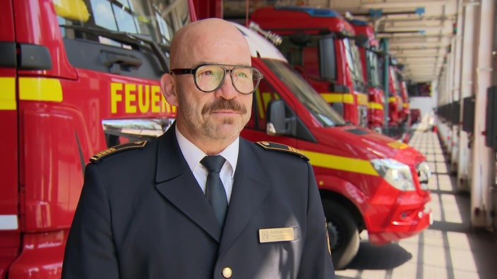 Andreas Klos der Feuerwehr Krefeld in Uniform vor den Einsatzwagen stehend.