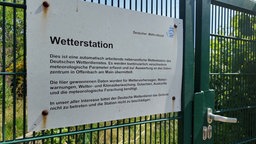 Schild einer Wetterstation vom Deutschen Wetterdienst an einem Zaun.