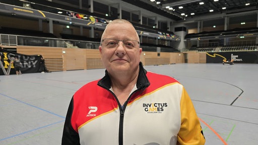 Ein Mann in einer Turnhalle stehend, gekleidet in einer Jacke der Invictus Games