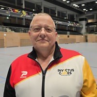 Ein Mann in einer Turnhalle stehend, gekleidet in einer Jacke der Invictus Games