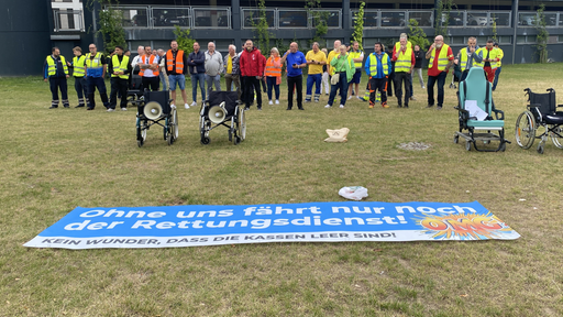 Eine Menschenkette steht hinter ein paar Rollstühlen und einem auf dem Boden liegenden Banner.