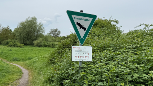 Ein Naturschutzgebietschild mit Verboten darunter steht auf einer grün bewachsenen Naturfläche. 