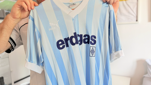 Ein blau-weißes Trikot wird in die Kamera gehalten.
