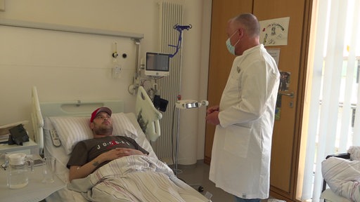 Oberarzt Udo Boeken steht am Krankenhausbett von Spenderherzempfänger Phil Kiss