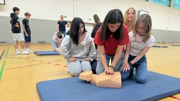 Dei Schülerinnen üben die Herz-Rhythmus Massage an der Übungspuppe