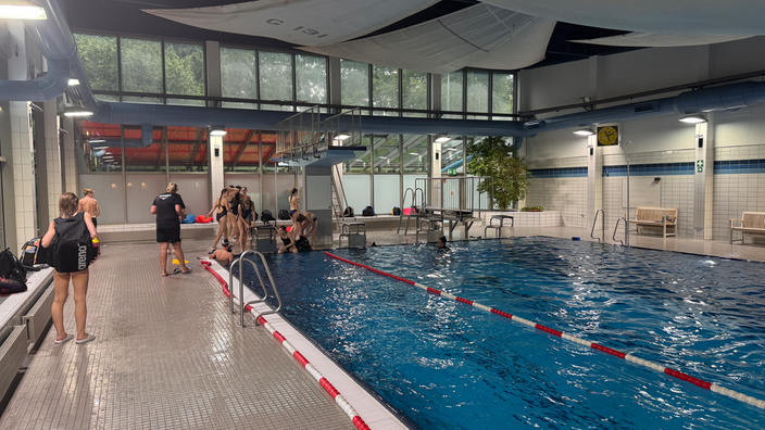 Ein großes Sportschwimmbecken mit Sprungturm und einigen jungen Schwimmern.
