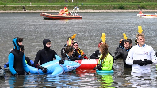 Teilnehmer des Rheinschwimmens gehen in den Rhein, kostümiert und mit Neopren-Anzügen.