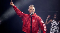 Robbie Williams in rotem Anzug auf der Bühne in Manchester
