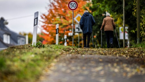 Rentner-Ehepaar spaziert im Herbst auf einem Gehweg