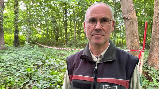 Stadtförster Stefan Jeschke steht vor einem weiß-roten Absperrband im Wald.