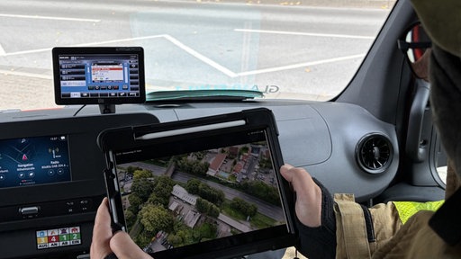 Ein Feuerwehrmann sitzt im Auto und sieht sich Flugbilder auf einem Tablet an