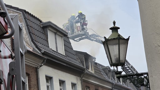 Rauch aus dem Dach eines Wohnhauses während zwei Feuerwehrmänner versuchen den Brand zu löschen