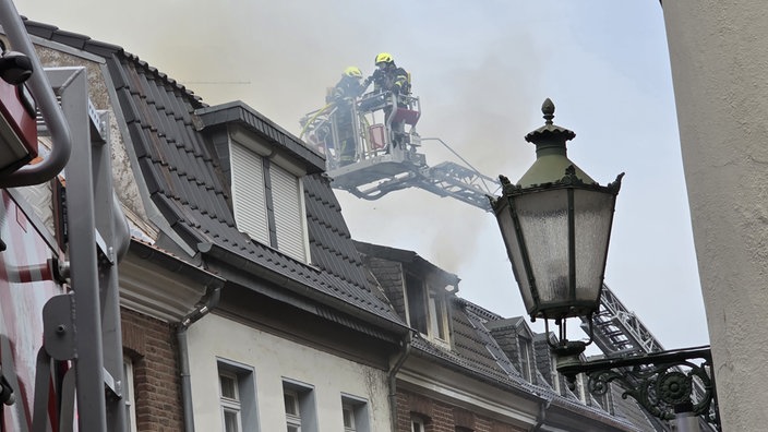 Rauch aus dem Dach eines Wohnhauses während zwei Feuerwehrmänner versuchen den Brand zu löschen
