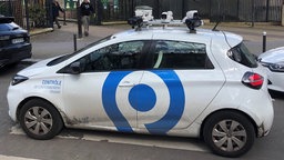 Ein kleines, weißes Auto mit Kameras auf dem Dach