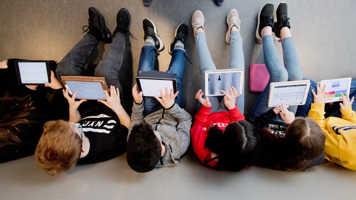 Schüler sitzen auf dem Boden mit ihren IPads und lernen