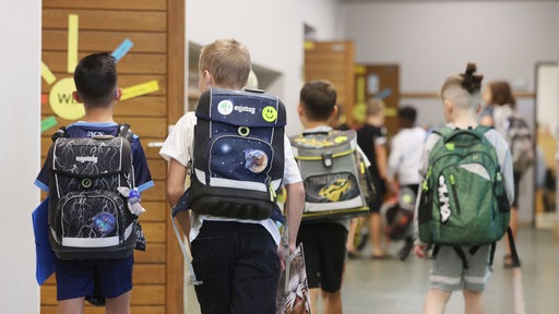 Kinder laufen mit ihrem Schulranzen auf dem Flur der Schule entlang