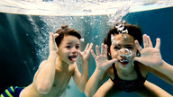Zwei Kinder tauchen unter Wasser und schneiden fröhliche Grimassen