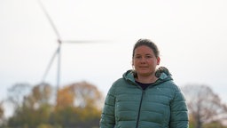 Kathrin Möllers steht in ihrem Garten. Im Hintergrund eines der aus ihrer Sicht problematischen Windräder. 