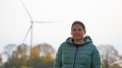 Kathrin Möllers steht in ihrem Garten. Im Hintergrund eines der aus ihrer Sicht problematischen Windräder. 