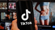 Tik Tok auf einem Smartphone vor einem Computerbildschirm, auf dem das Bild einer schlanken Frau zu sehen ist