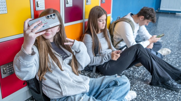 Eine Gruppe Jugendlicher mit Smartphones vor Schließfächern