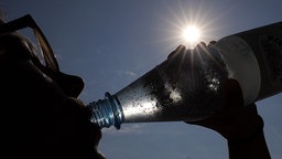 Eine Frau trinkt in der Sonne Mineralwasser.