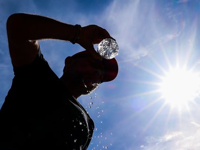 Nordrhein-Westfalen, Düsseldorf: Ein Mann trinkt bei sommerlichen Temperaturen aus einer Wasserflasche und schüttet sich Wasser über sein Gesicht.