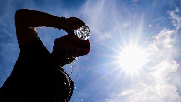 Nordrhein-Westfalen, Düsseldorf: Ein Mann trinkt bei sommerlichen Temperaturen aus einer Wasserflasche und schüttet sich Wasser über sein Gesicht.
