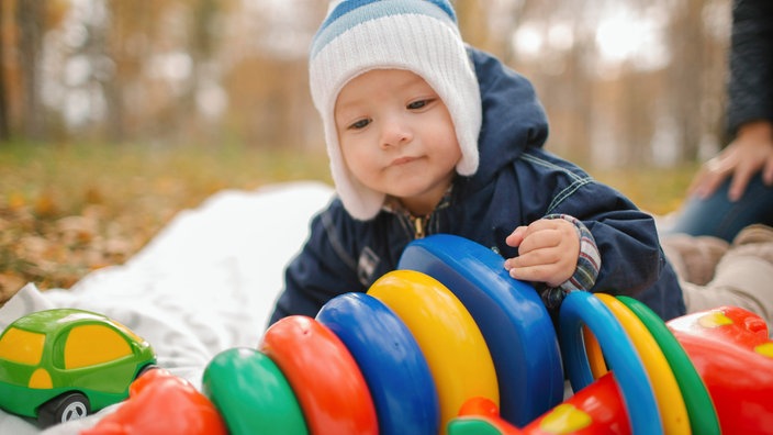 Ein kleines Baby kriecht zu einem bunten Plastikspielzeug.