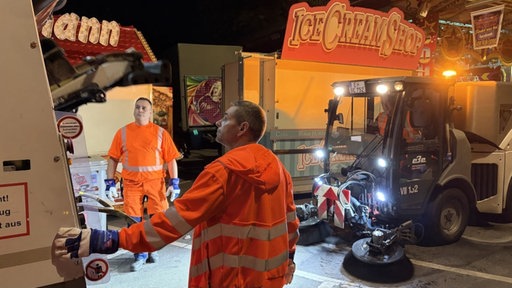 Zwei Mitarbeiter der Straßenreinigung in Essen schauen in den Müllwagen.