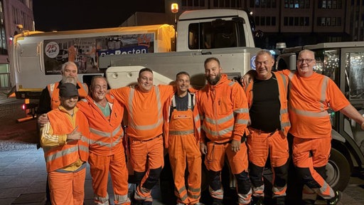 Das Team der Straßenreinigung in Essen schaut in ihren orangenen Klamotten bei Nacht in der Kamera.