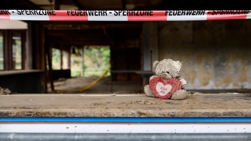 Ein Teddybär sitzt verwahrlost unter einem Feuerwehrabsperrband
