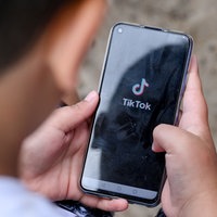Ein Junge hält ein Smartphone in der Hand, auf dem das TikTok Logo zu sehen ist