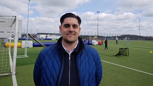 Trainer Tobias Schnäbeli, junger Mann mit dunklen Haaren und einer blauen Jacke, steht auf einem Fußballfeld