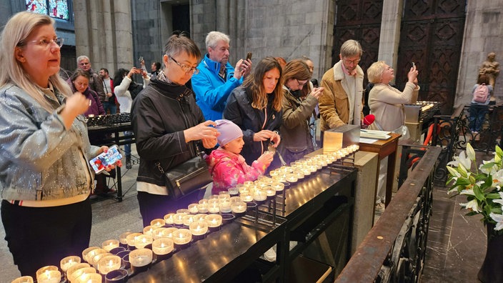 Menschen zünden Kerzen an für den Papst im Kölner Dom