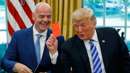 Donald Trump hält eine rote Karte in der Hand, während einem Treffen mit FIFA-Chef Gianni Infantino
