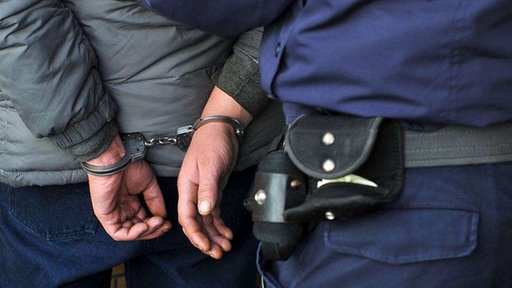 Ein Polizist führt eine Person in Handschellen ab