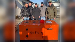 Fünf Männer stehen vor einem orangenen Container mit der Aufschrift "New Boy"