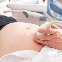 Eine Schwangere liegt auf einem Untersuchungsstuhl und ein Ultraschallgerät wird über ihren Bauch gefahren