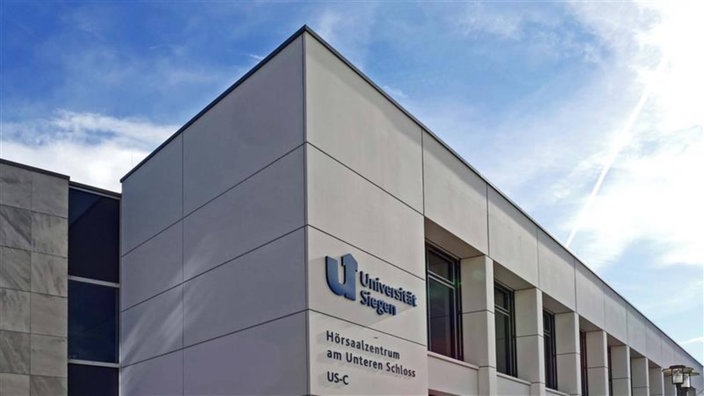 Ein leerer Hörsaal mit blauen Sitzreihen, unten ein Tisch und eine große Leinwand