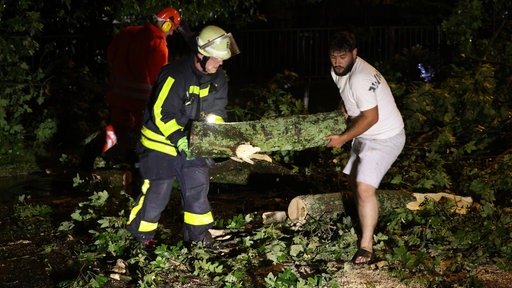 Feuerwehrmänner und ein Anwohner arbeiten an der Beseitigung von umgewehten Bäumen in Krefeld
